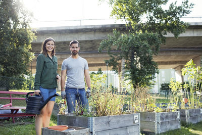 Portrait of happy mid adult couple with watering can in urban garden