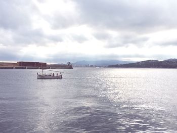 Boat sailing in sea against cloudy sky