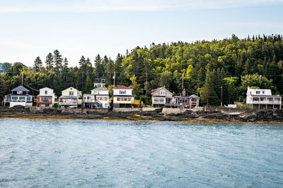 Houses by river against buildings and trees against sky