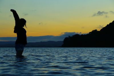 Silhouette man in sea against sky during sunset