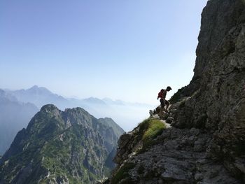 Hiker climbing rocky mountains against clear blue sky
