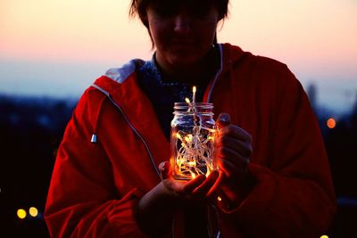 Midsection of woman holding lighting equipment during sunset