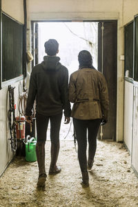 Full length rear view of young couple walking in horse stable