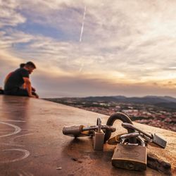 Man sitting on metal against sky during sunset