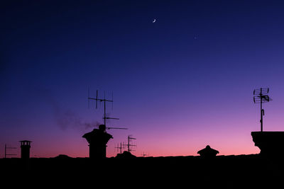 The last rays of the sun. the moon above a silhouette of houses with chimneys and antennas.