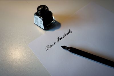 Close-up of paper with fountain pen and ink bottle on table