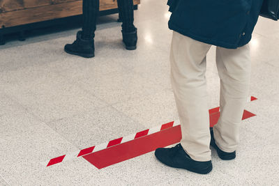 Low section of man standing next to the red warning markings on light floor