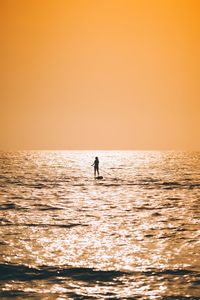 Silhouette man in sea against orange sky