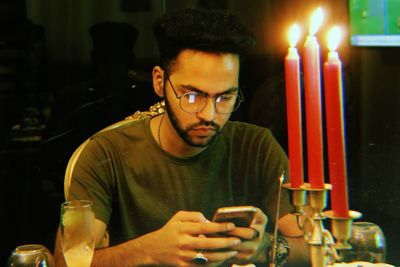 Man using mobile phone by lit candles in restaurant