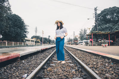 Portrait of young woman standing on railroad track against sky