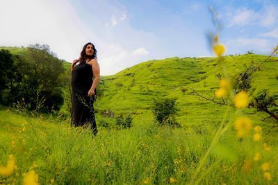 Full length portrait of young woman standing on field against sky