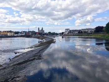 Bridge over river by buildings in city against sky