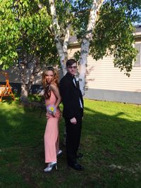 Full length of cheerful teenage couple standing on grassy field at yard during prom