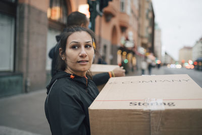 Thoughtful woman carrying box while walking with coworker in city during delivery