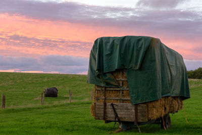 Hay bales on field against sky during sunset