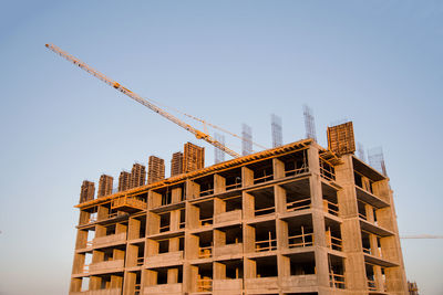 Low angle view of crane by building against clear sky