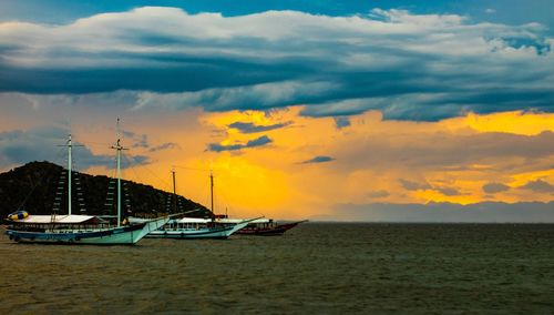 Sailboats moored in sea against sky during sunset