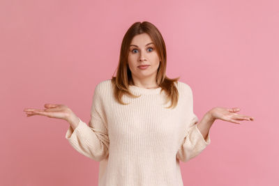 Portrait of young woman standing against pink background