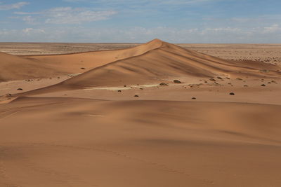 Scenic view of sand dunes in desert against cloudy sky