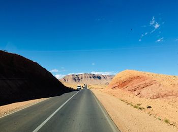 Empty road by mountain against blue sky