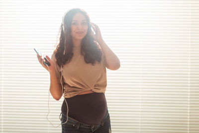 Young woman using phone while standing against wall