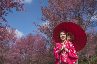 Smiling woman with umbrella standing against trees