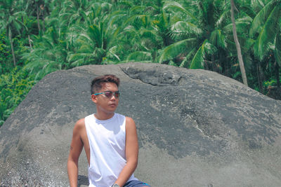 Young man wearing sunglasses sitting on rock