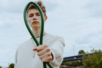 Portrait of confident man holding garden hose against sky
