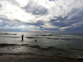 Silhouette woman in sea against cloudy sky