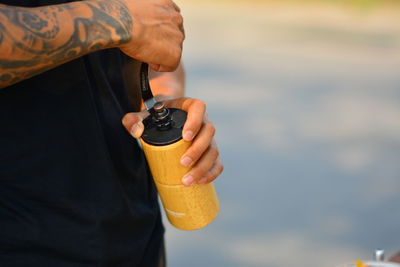 Midsection of man holding bottle while standing outdoors