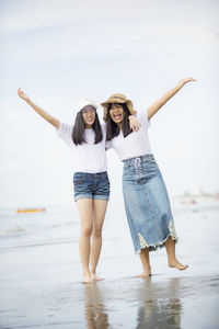 Full length of happy friends standing at beach against sky