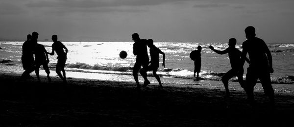 Silhouette people playing soccer at beach during sunset