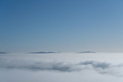 Low angle view of clouds from above under a blue sky with mountain peaks in the distance