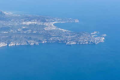 Aerial view of sea by mountain against blue sky