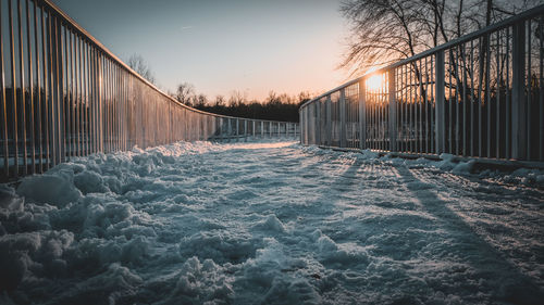 Snow covered bridge against sky during sunset