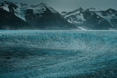 Scenic view of sea by snowcapped mountain against sky