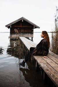 Side view of woman sitting on wooden pier at lake