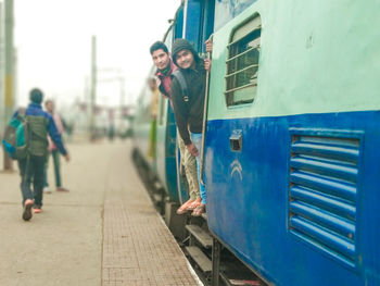 Portrait of friends standing on train doorway at railroad station platform