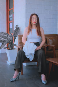 Portrait of woman sitting on chair against wall