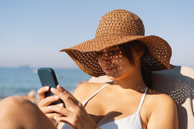 Young woman using mobile phone while standing against sky