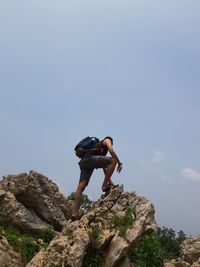 Low angle view of man standing on rock against sky