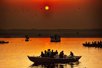 Silhouette people in sea against sky during sunset