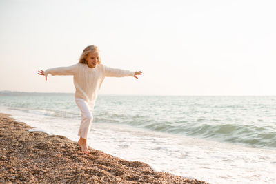 Happy smiling kid girl 5-6 year old wear knit sweater and pants running over sea shore outdoors.