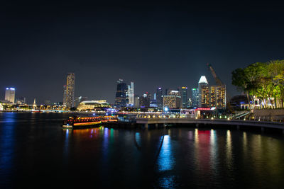 Illuminated buildings by river against sky at night