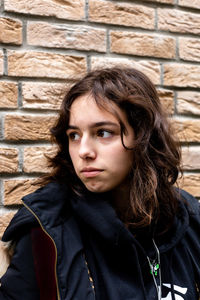 Portrait of teenager girl in front of bricks wall. black wearing teen looking aside
