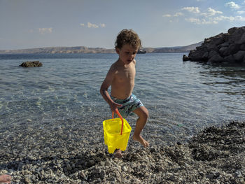 Little boy carrying a brigh yellow pale of water near the sea