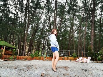 Side view portrait of young woman standing against trees