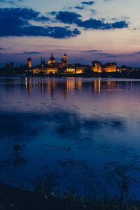 Illuminated buildings at waterfront during sunset