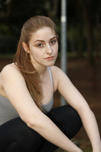 Portrait of confident young woman crouching at park