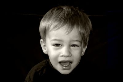Portrait of boy with mouth open against black background